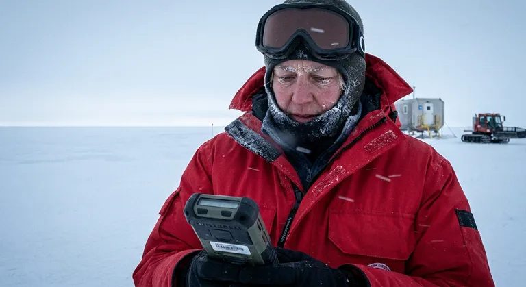 A medium shot of a woman in her 50s, a scientist, at a research station in Antarctica, outside in the full cold, face wr…